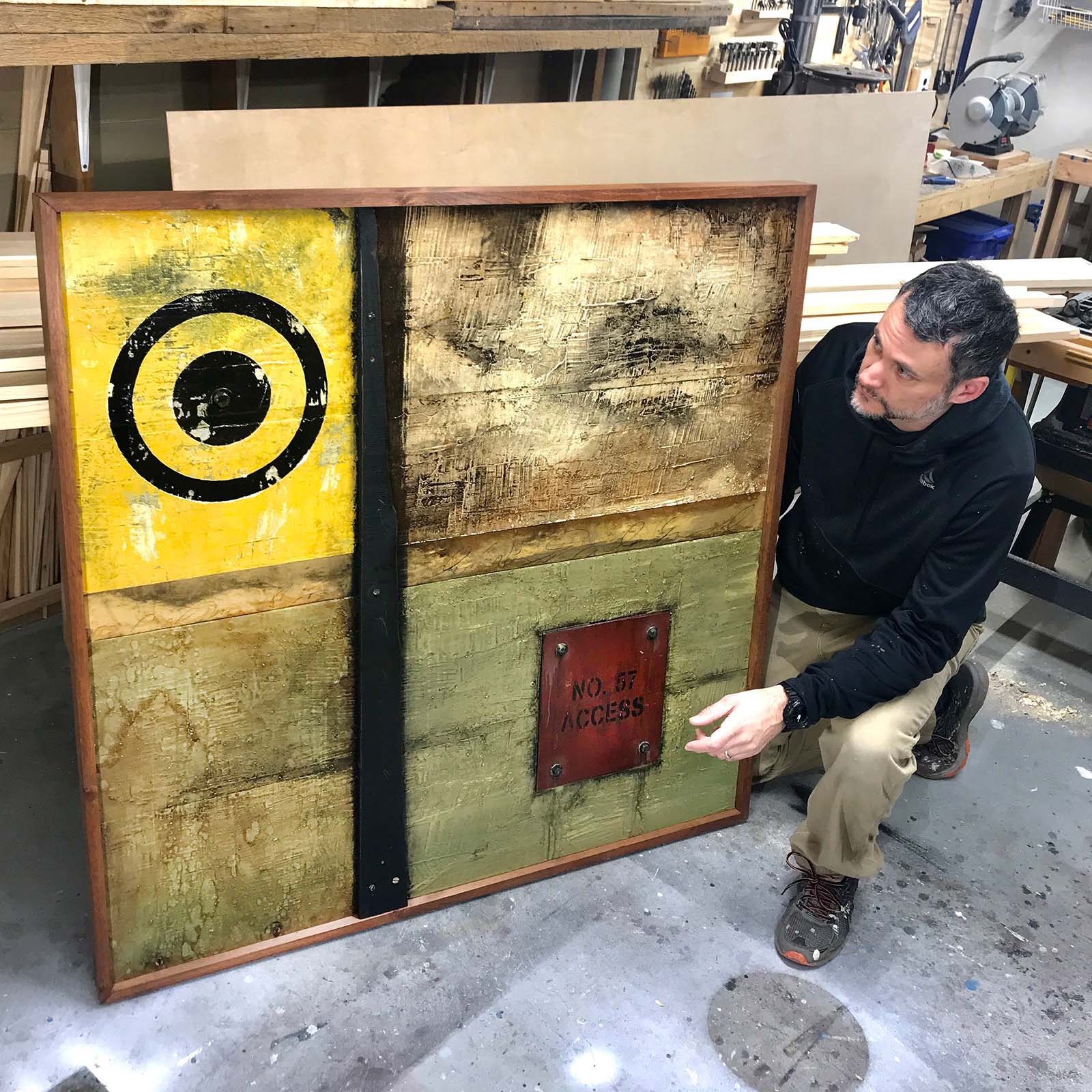 Artist Domenick Naccarato kneeling beside one of his larger works from his Wall Segments & Markings series.