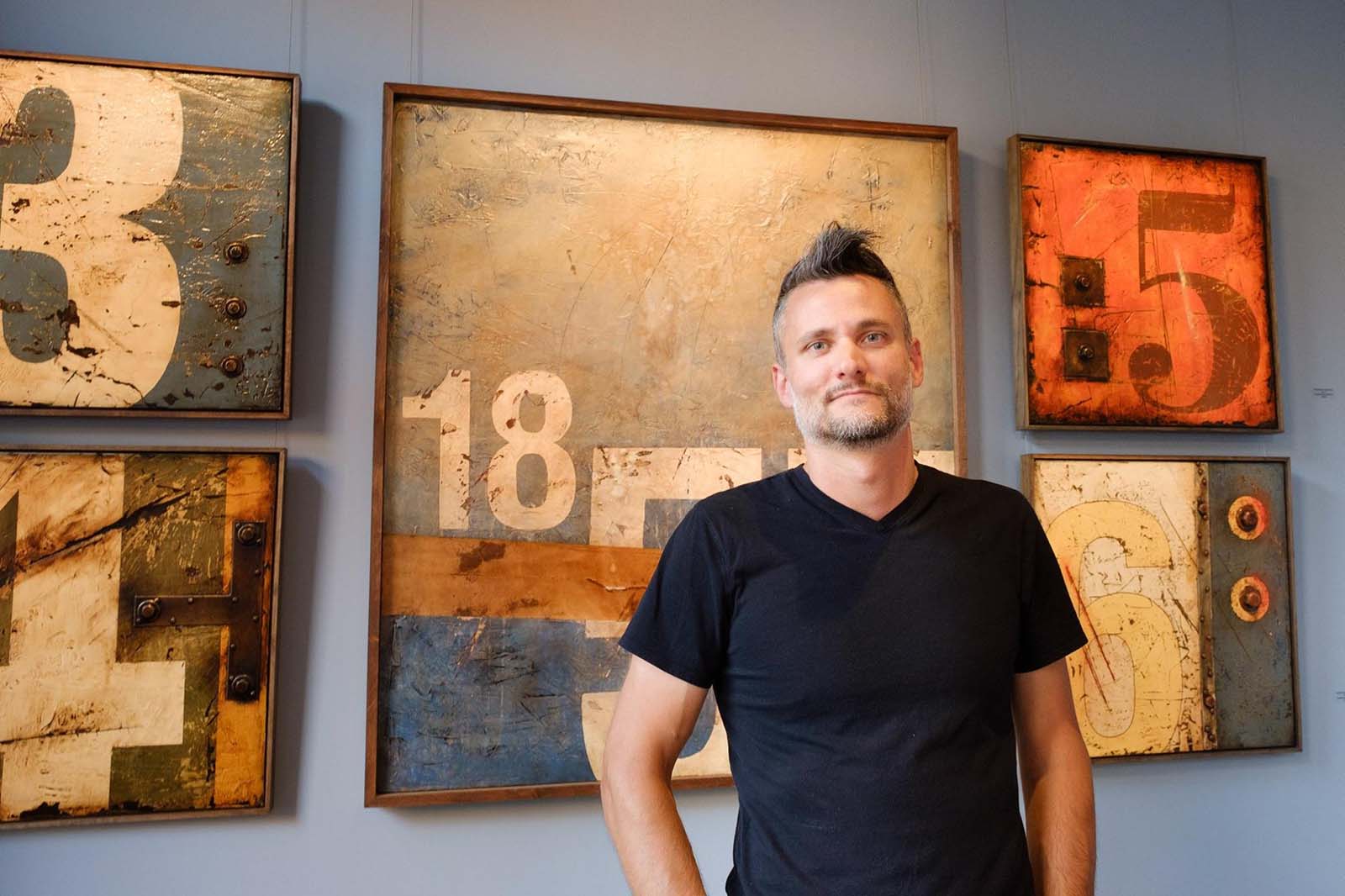 Artist Domenick Naccarato standing in front of a display of his work hanging at the Bethlehem House Gallery in Bethlehem, PA.